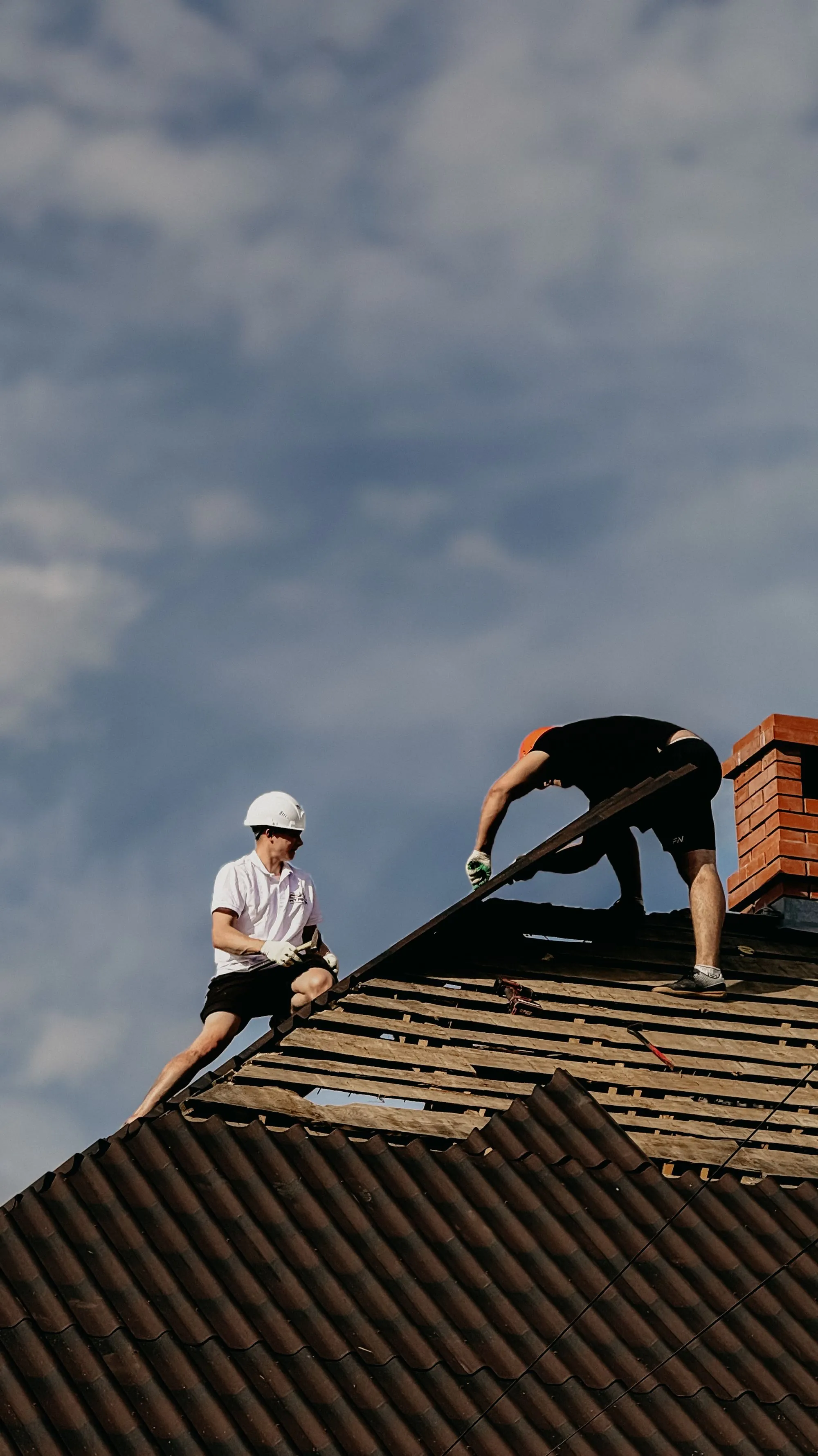 Two roofers stripping an old covering back beside a brick chimney
