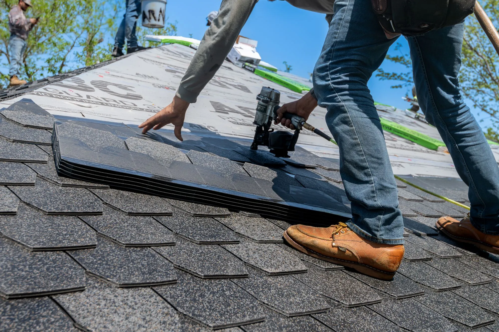 A roofer setting a bundle of shingles down on a prepared slope
