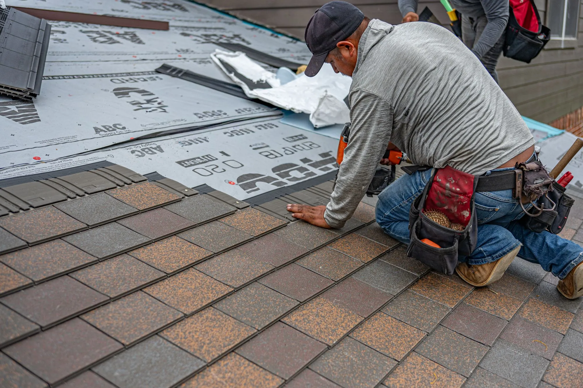 A roofer kneeling to lay a course of shingles over underlayment