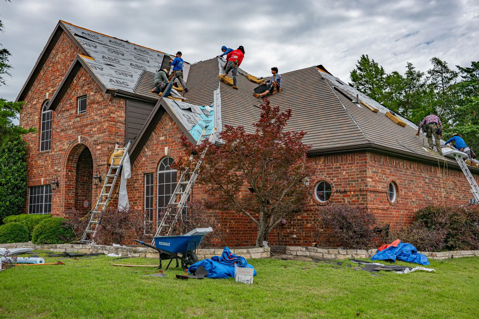A crew re-covering the long roof of a large brick house