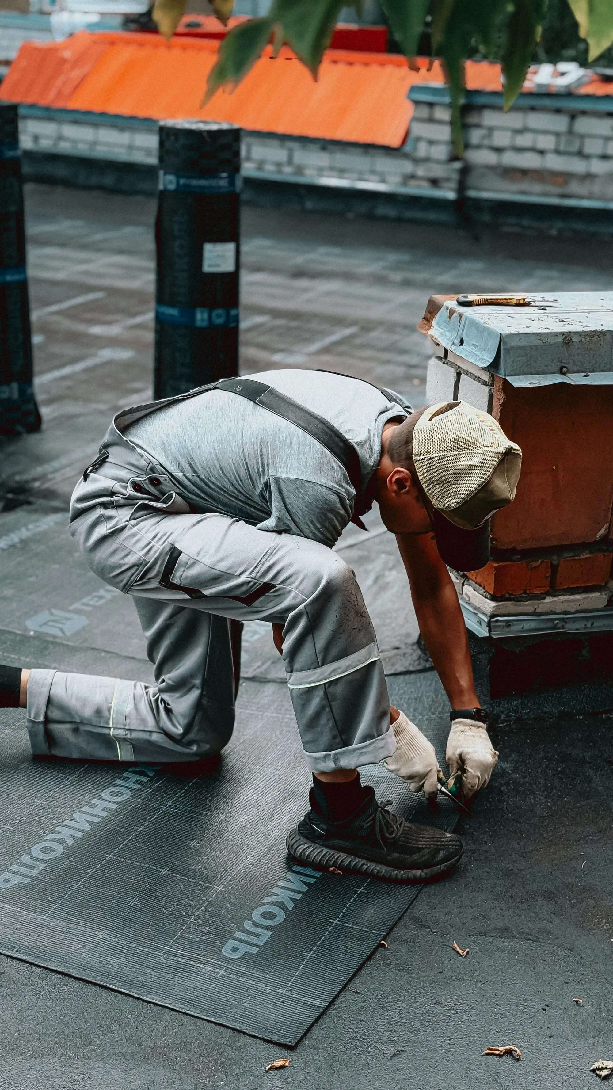 A roofer bending to work on the flashing beside a chimney