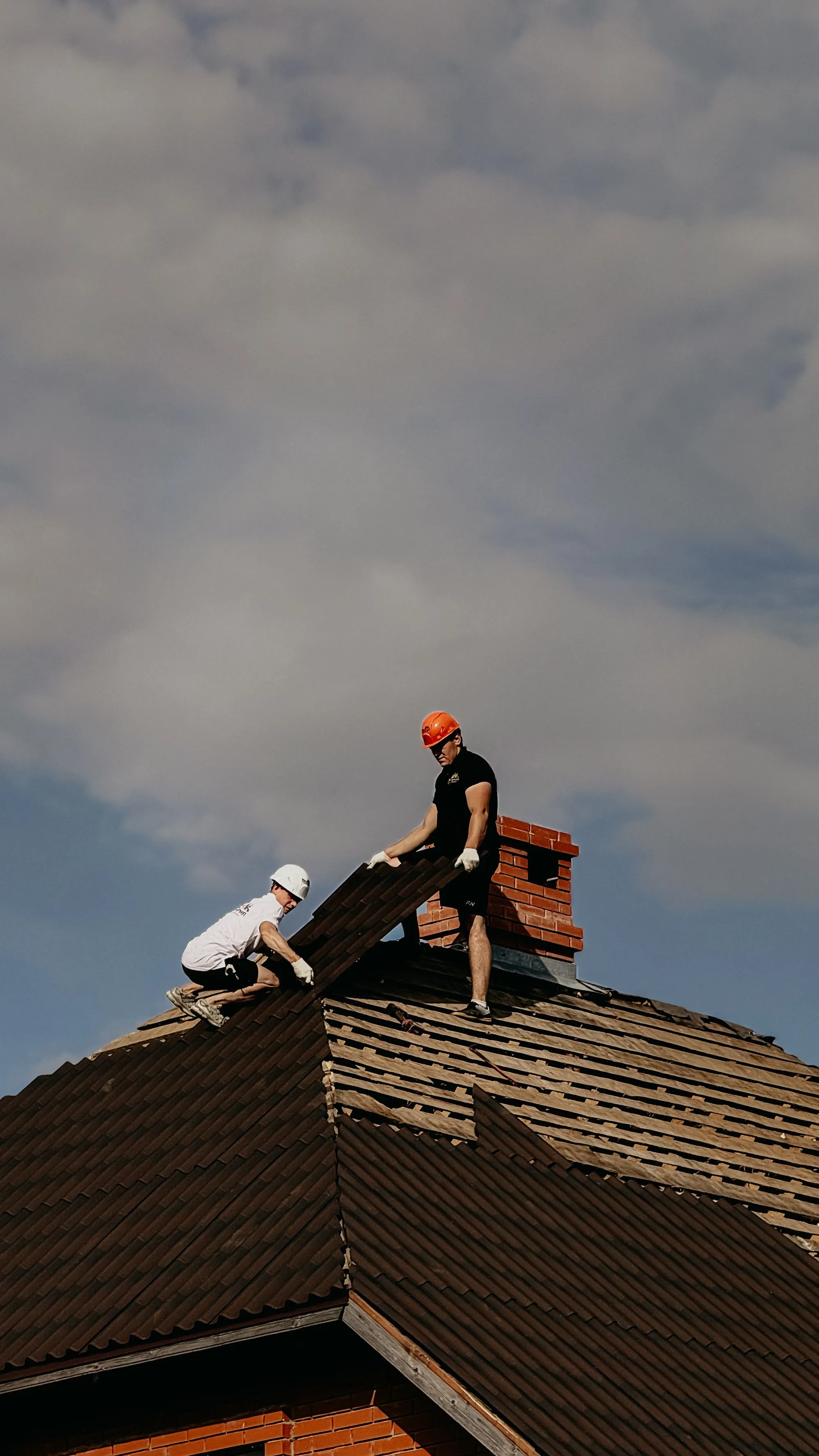 Two roofers lifting an old covering away beside a brick chimney