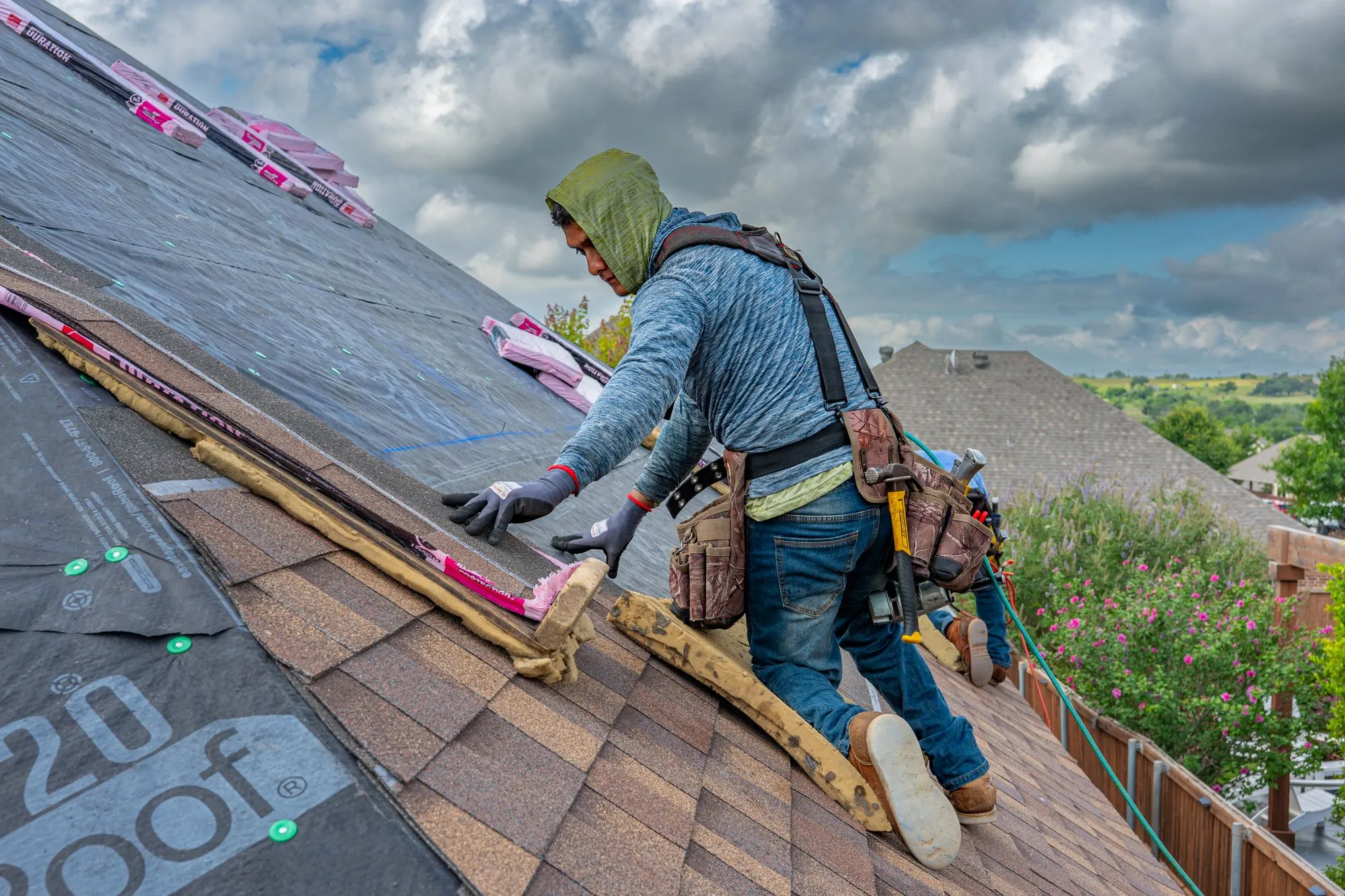 A roofer working a run of shingles across a slope