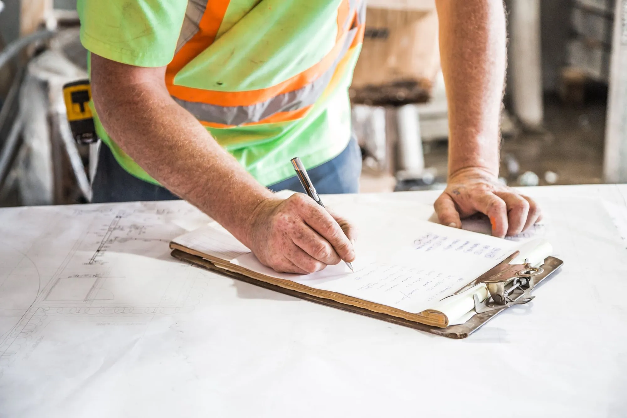 A worker in a high-visibility vest writing on a clipboard